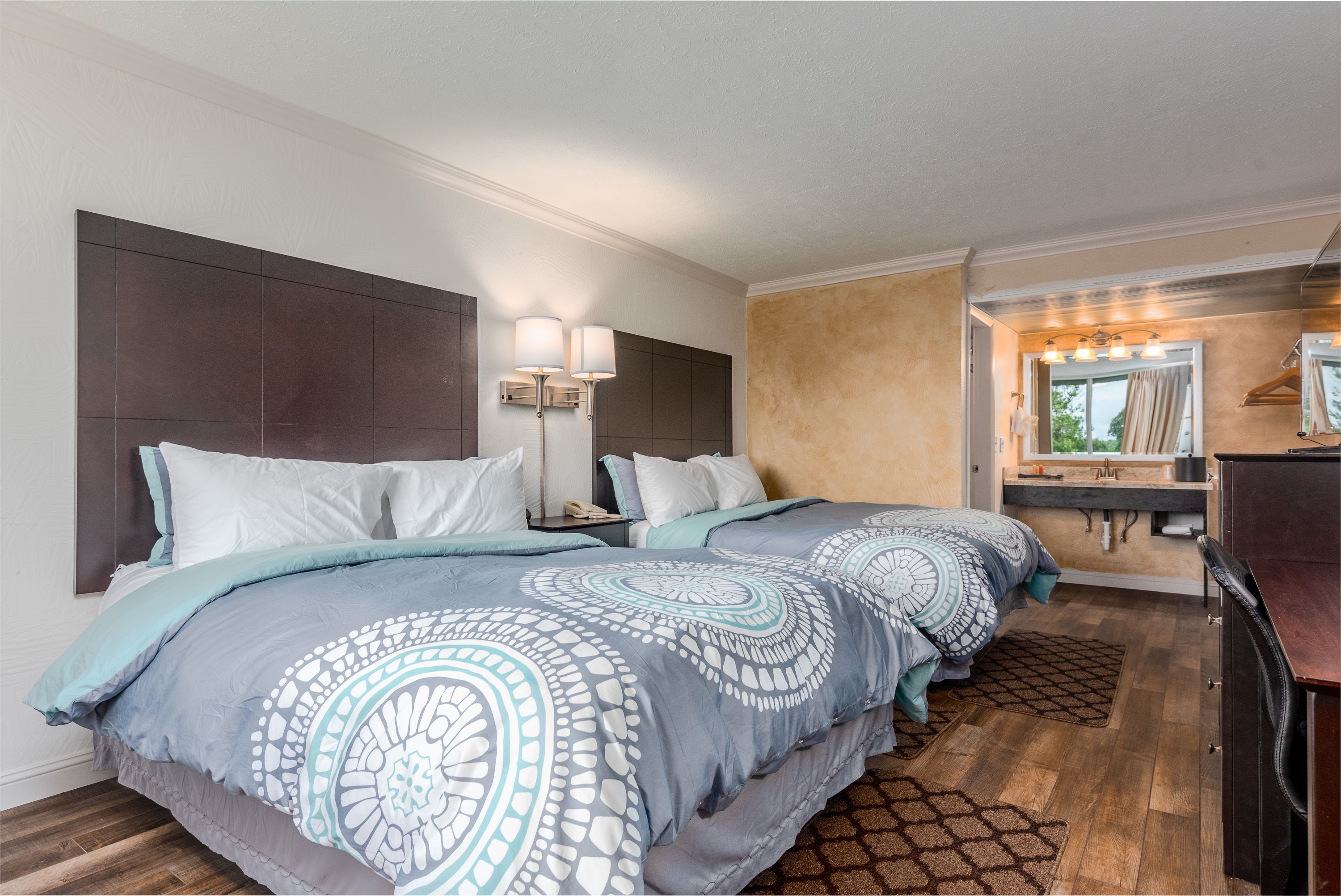 Quarto de hotel com duas camas, uma toucador com espelho e chão de madeira.
