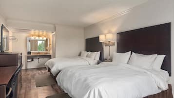 Habitación de hotel con dos camas, un escritorio, una tocador con espejo y una ventana con cortinas.