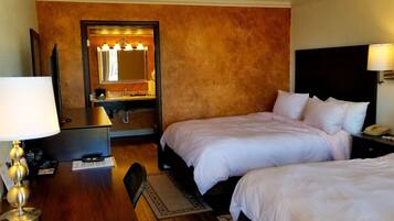 Habitación de hotel con dos camas, un escritorio con lámpara, tocador con espejo y teléfono en la mesita de noche.