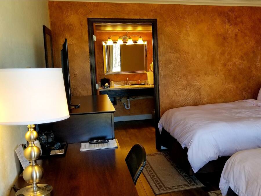 Habitación de hotel con dos camas, un escritorio con lámpara, tocador con espejo y teléfono en la mesita de noche.