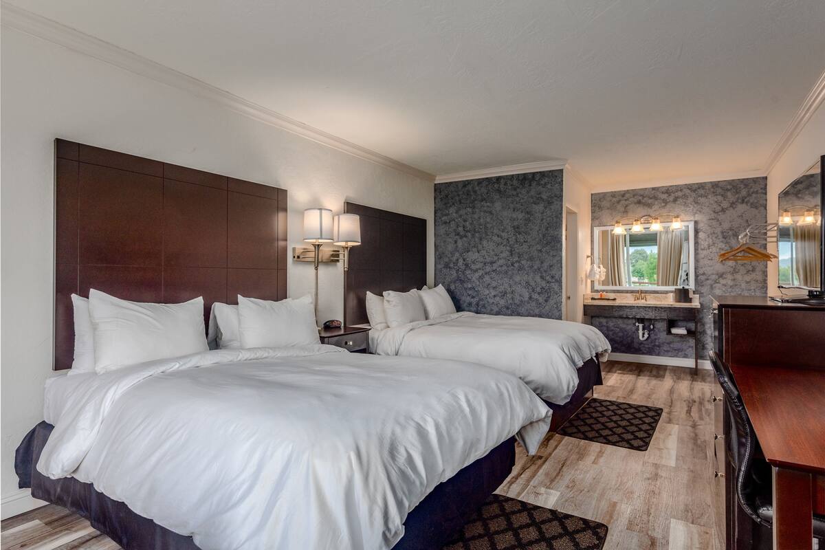 A hotel room with two beds, a large mirror, a vanity with a sink, and a wooden floor.