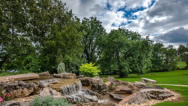 Un jardín con una pequeña cascada, rodeado de rocas y follaje.
