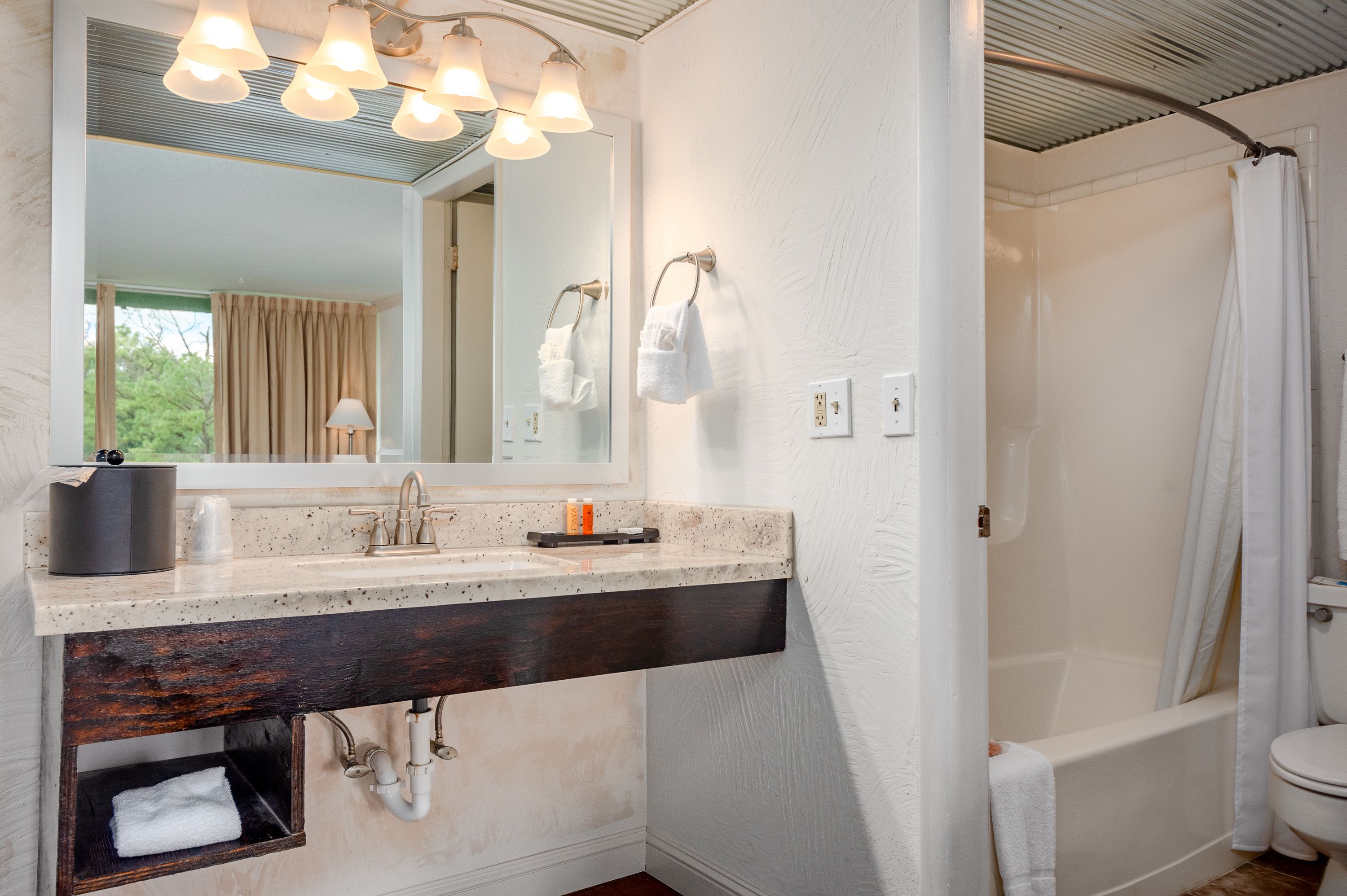 A bathroom with a large mirror, a sink with a dark wooden base, a bathtub, and a shower curtain.