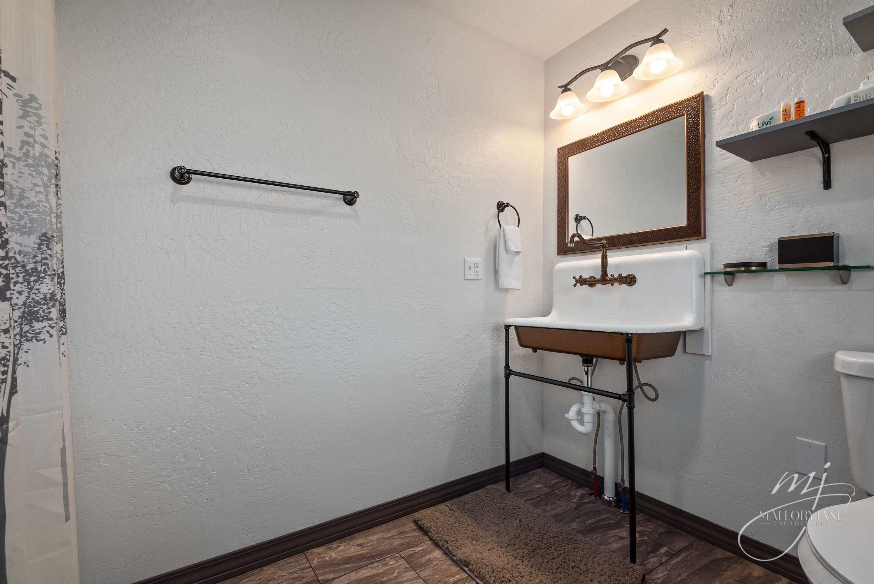 Ein Badezimmer mit einem weißen Waschbecken, einem beleuchteten Spiegel, einem Handtuchhalter und einer Duschkabine.