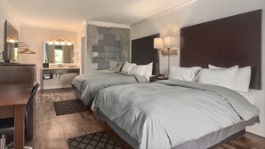 Habitación de hotel con dos camas, un escritorio, un espejo, un tocador con lavabo y una pared decorativa de piedra.