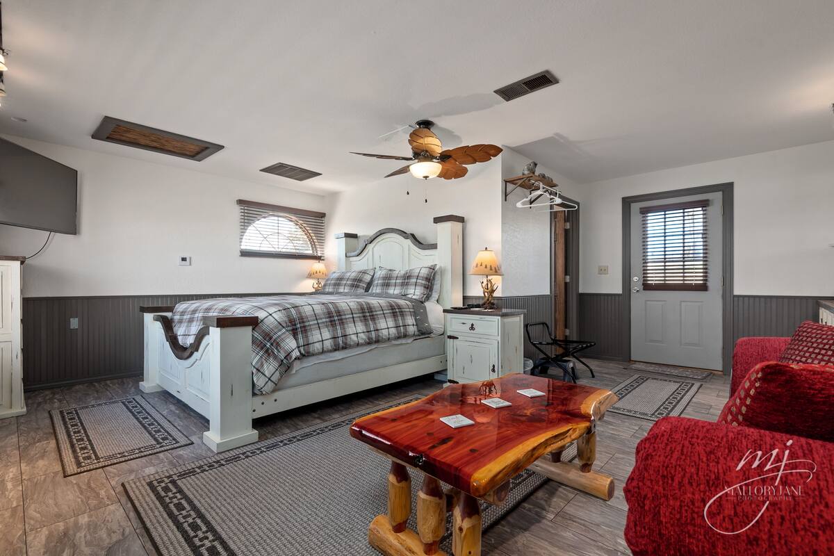 A bedroom with a bed, bedside tables, a wooden bench, a ceiling fan, and a window with blinds.