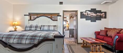 Een slaapkamer met een bed, een rode bank, een houten salontafel en een kunstwerk aan de muur.
