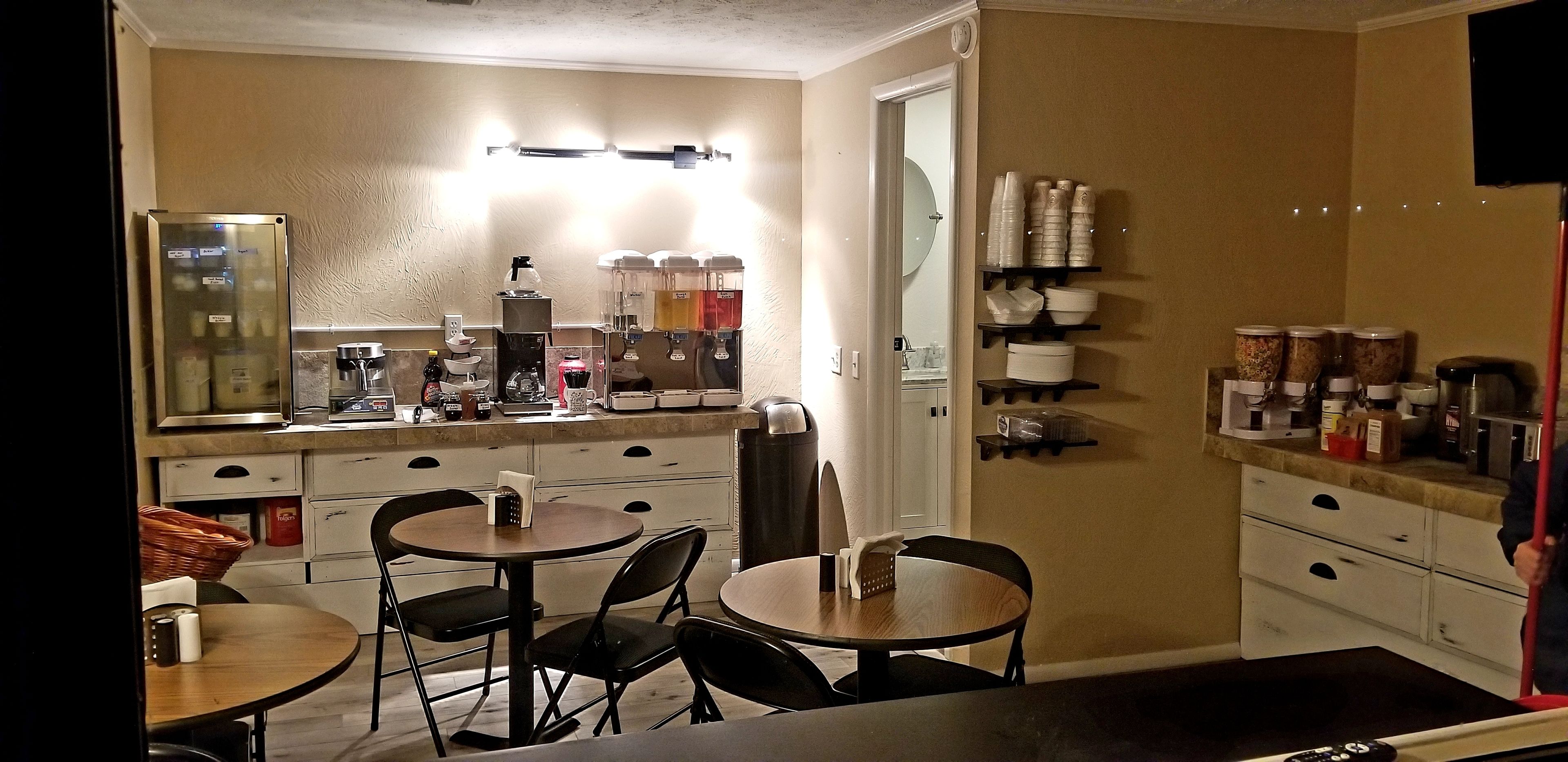 A compact kitchen with a refrigerator, coffee maker, and various storage containers. There are two dining tables with chairs.