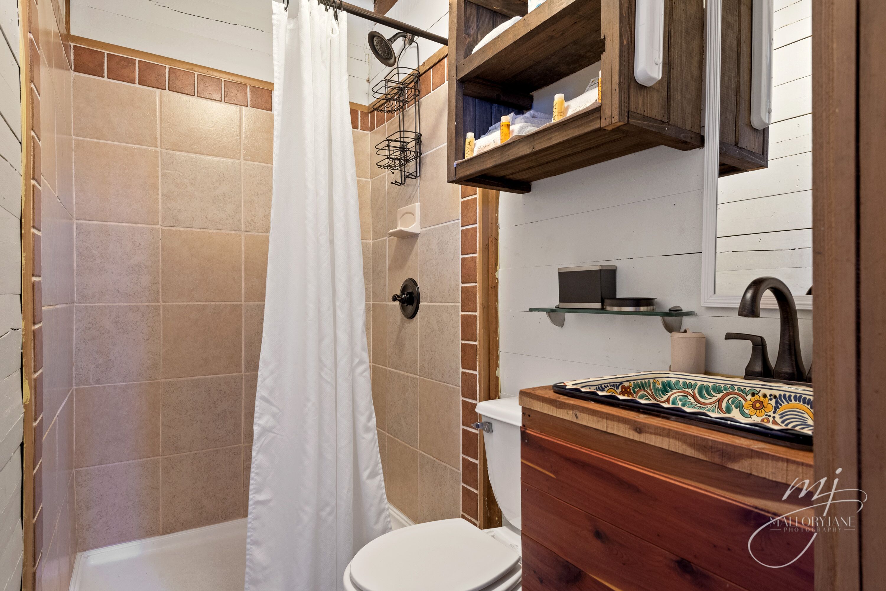 Un baño con ducha, inodoro y tocador de madera con salpicadero de azulejos.