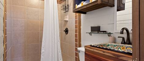 Un baño con ducha, inodoro y tocador de madera con salpicadero de azulejos.