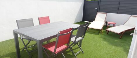 A patio with a table and chairs, a small table, and lounge chairs.