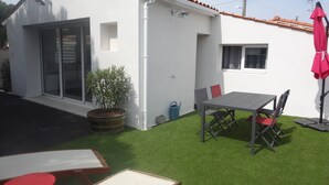 A small white building with a tiled roof, a sliding glass door, a window, and a patio area with a table and chairs. - Pretty little house in La Tremblade (La Tremblade)