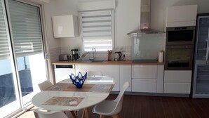 A modern kitchen with white cabinets, a built-in oven, and a dining area with a round table and chairs. - Pretty little house in La Tremblade (La Tremblade)