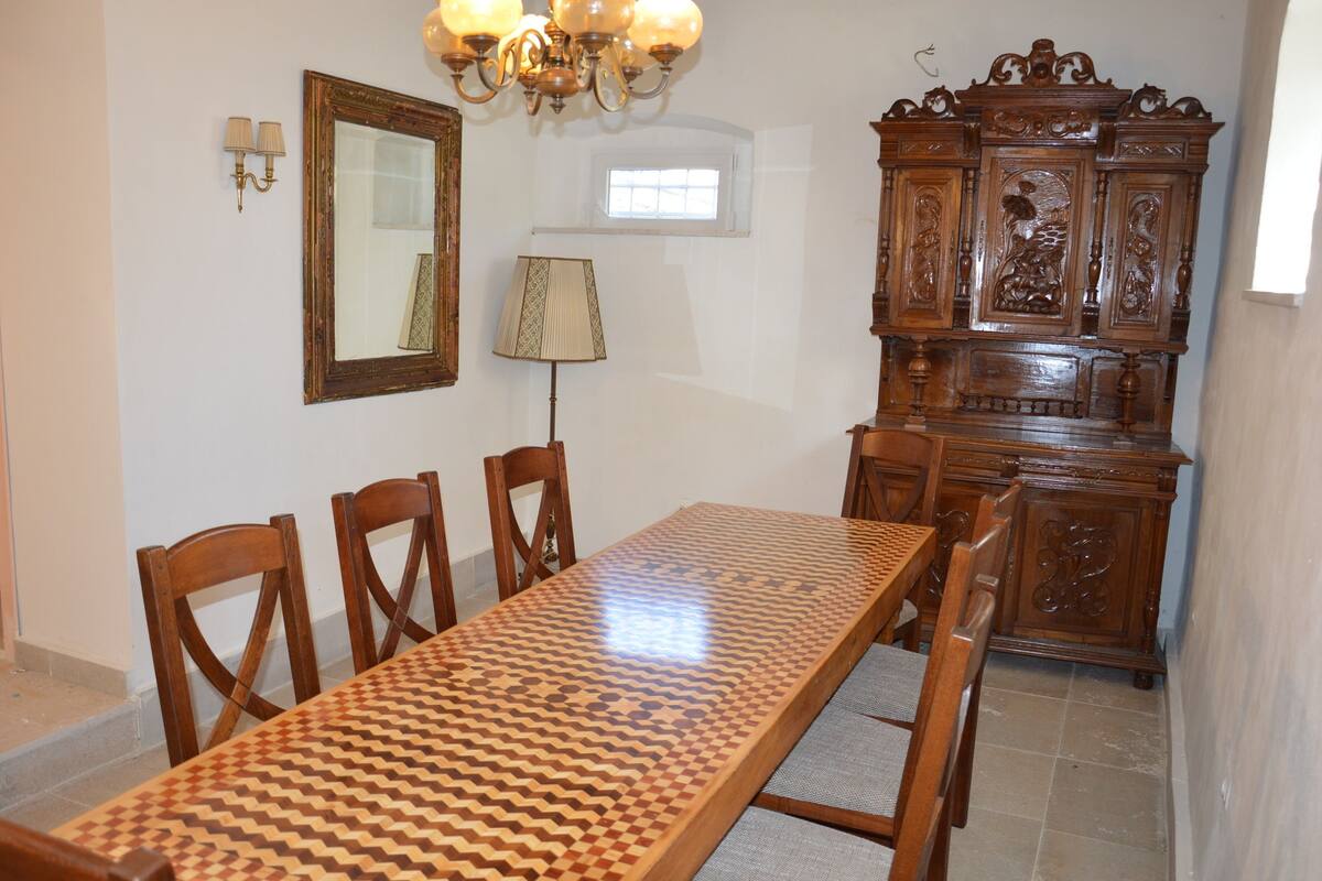 A dining area with a wooden table and chairs, a chandelier, a mirror, and a wooden cabinet.