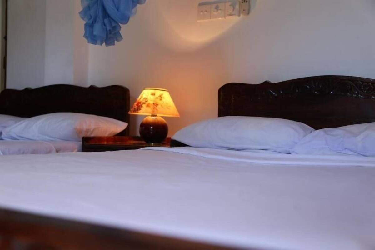 Una habitación de hotel con dos camas, una mesita de noche con una lámpara y una pared con un cuadro.