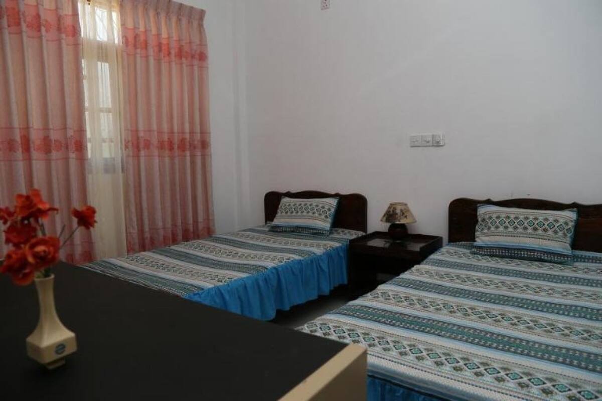 Una habitación con dos camas individuales, una mesita pequeña y un florero con flores.
