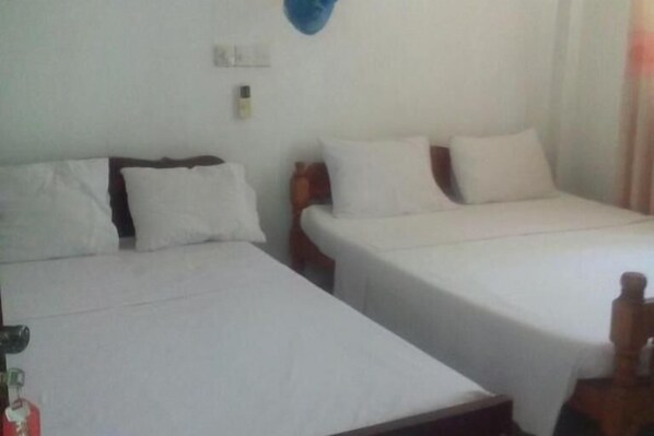 A simple room with two single beds, each with white bedding and wooden headboards. There is a small table with a bottle on it, and a wall-mounted light fixture above the beds.