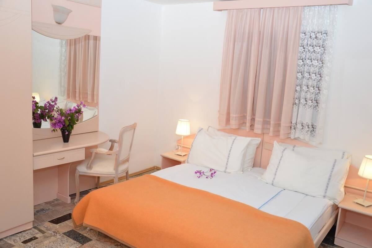 A hotel room with a bed, a desk, a chair, a nightstand, and a window with curtains.