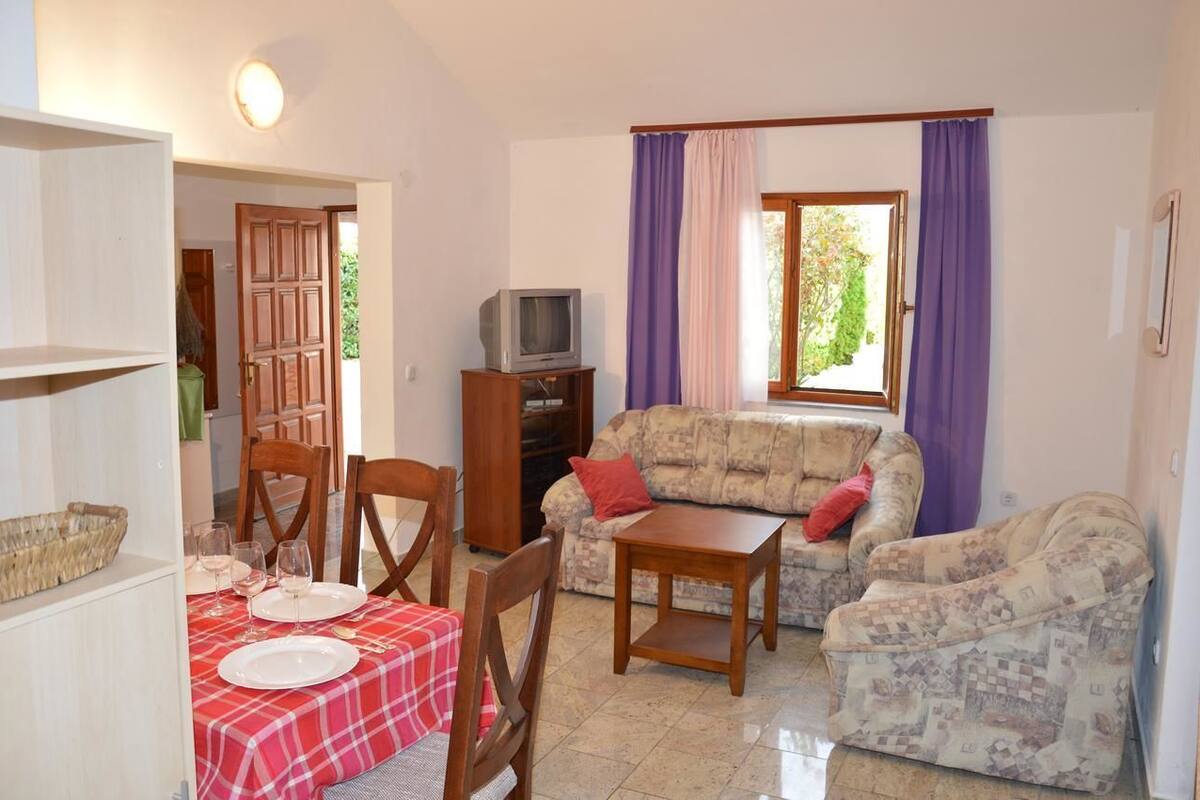 A living room with a sofa, chairs, a small table, and a television. There is a dining area with a table set for two.