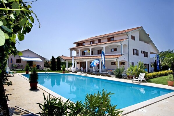 A large building with a swimming pool, multiple balconies, and outdoor seating.