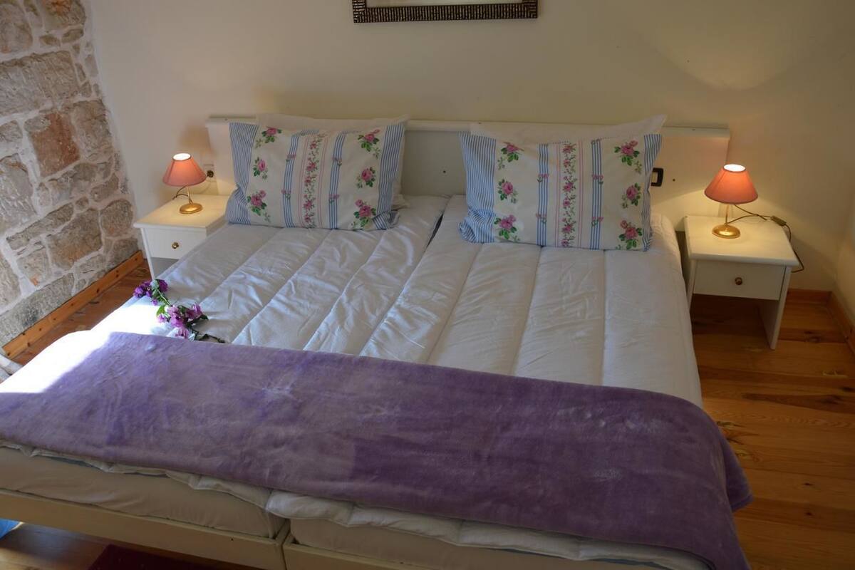 A double bed with floral bedding, two bedside tables with lamps, and a stone wall.