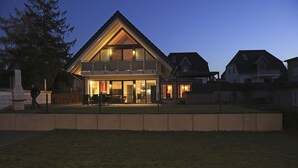 Une maison à deux étages, dotée d’un toit triangulaire imposant, d’un balcon et d’une entrée bien éclairée.
