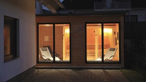 Une maison moderne dotée de deux grandes portes vitrées qui donnent sur un intérieur en bois ; chaque porte est agrémentée d’une chaise blanche à l’intérieur.