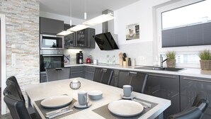 Une cuisine moderne avec un coin repas, comprenant un grand îlot central, des appareils électroménagers intégrés et une vue sur la ville.
