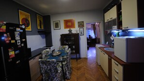 A compact kitchen with a dining area, wooden flooring, and a refrigerator with magnets. - Apartment 99 Muses (Belgrade)