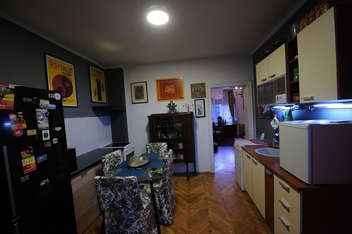A compact kitchen with a dining area, wooden flooring, and a refrigerator with magnets.
