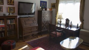A living room with a television, wooden furniture, a patterned rug, and a window with curtains. - Apartment 99 Muses (Belgrade)