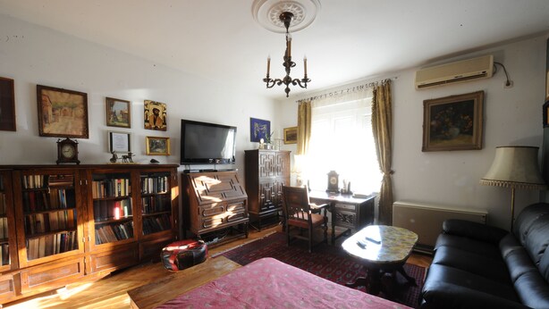 A living room with a television, bookshelves, a sofa, a small table, and a patterned rug. - Apartment 99 Muses (Belgrade)