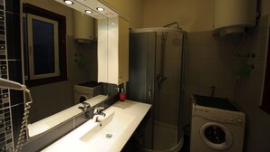 A bathroom with a sink, mirror, shower, and washing machine. - Apartment 99 Muses (Belgrade)