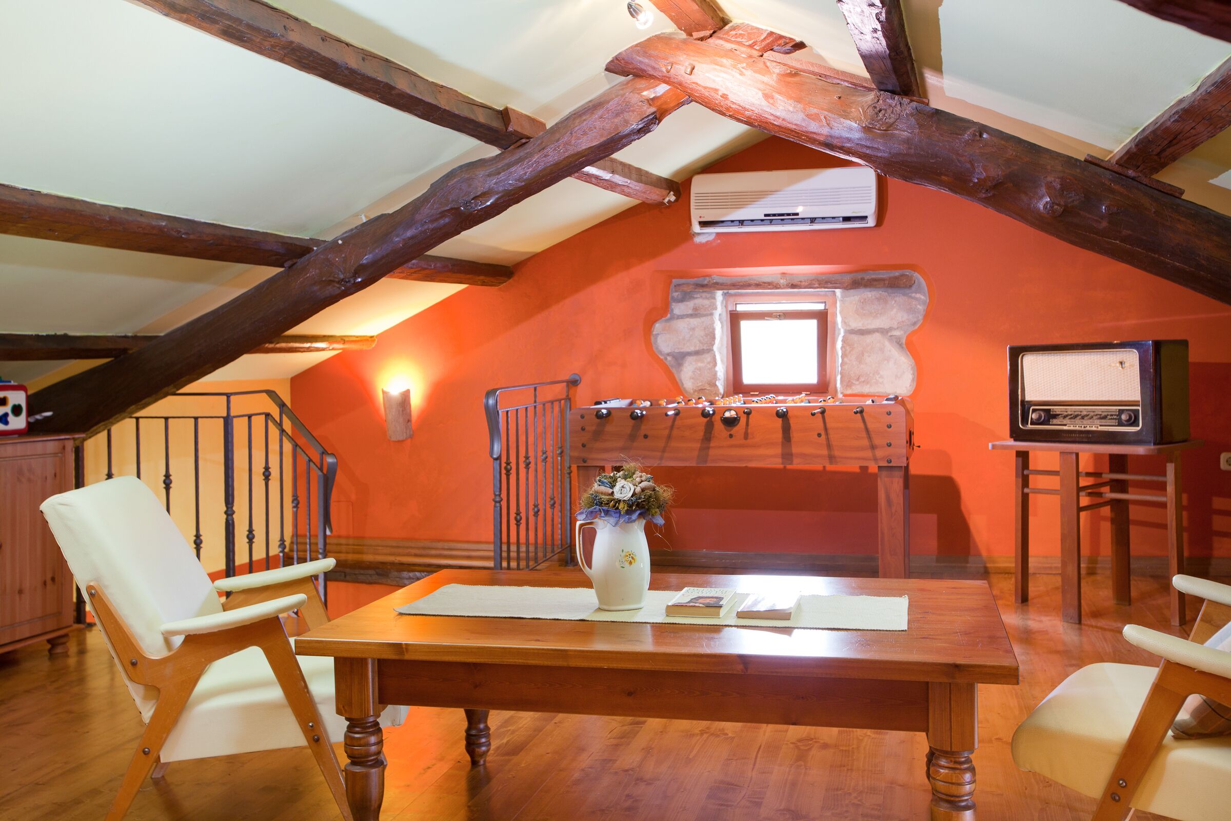 A cozy room with a wooden table, two chairs, a vase with flowers, a television, and a staircase with a railing.