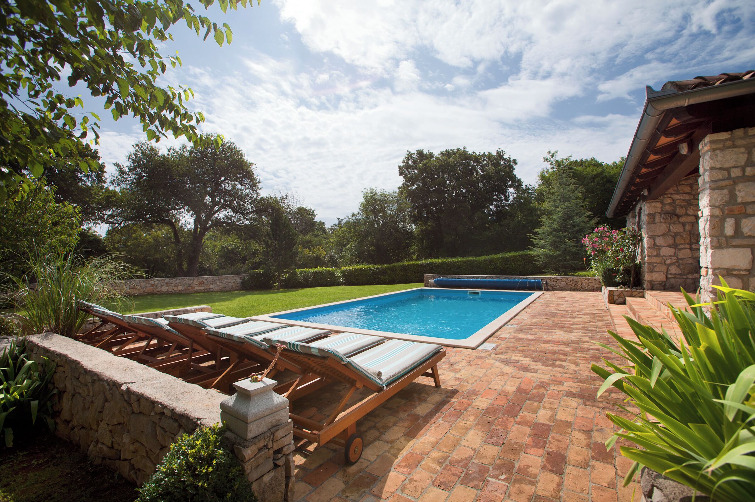 A backyard with a swimming pool, lounge chairs, and a stone wall.