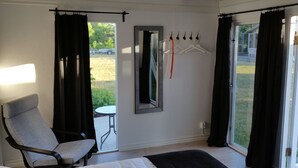 Ein Zimmer mit Bett, Stuhl, Tisch, Spiegel und einem Fenster mit Vorhängen.