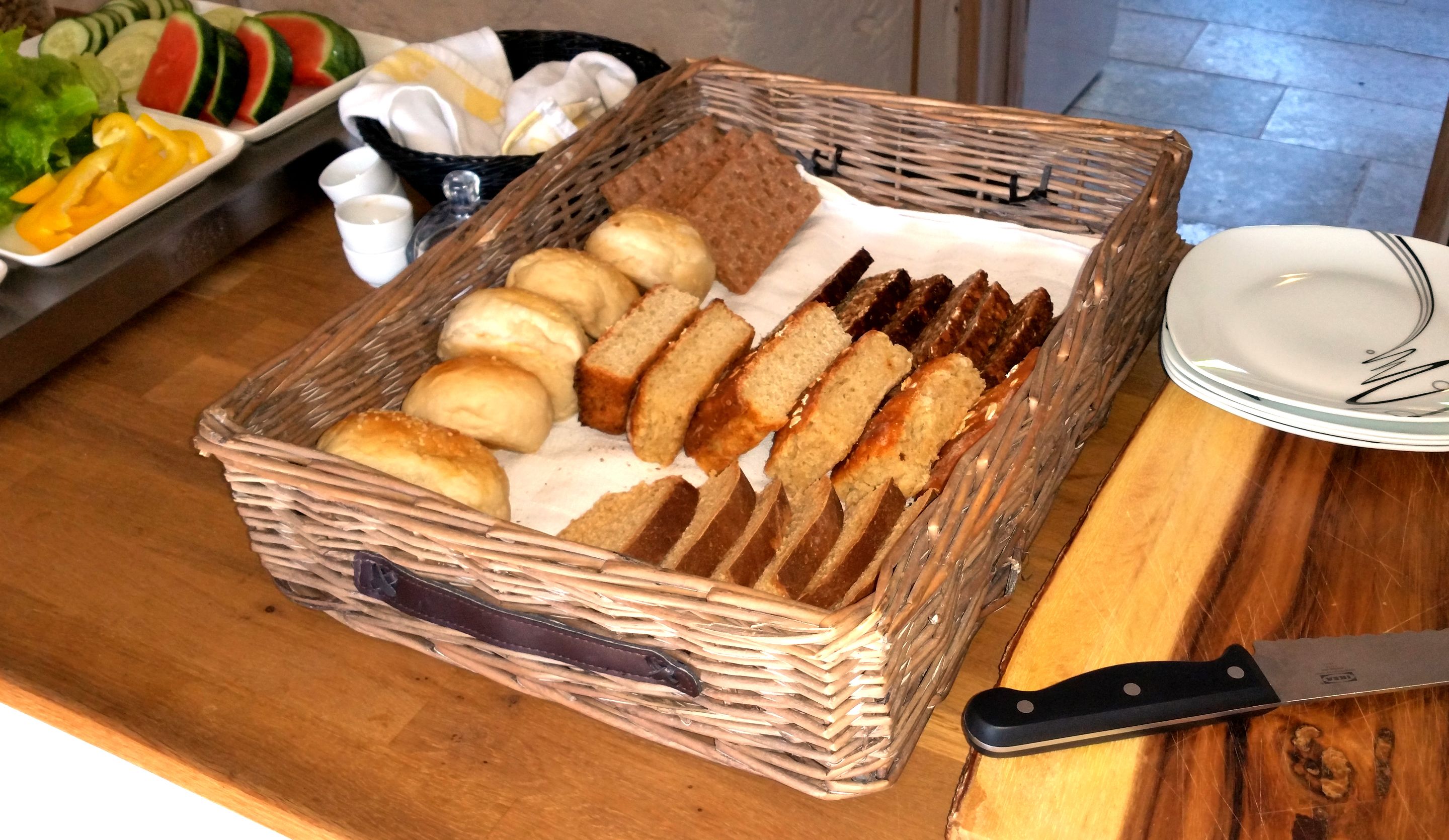 A wicker basket filled with various breads and rolls on a wooden table.
