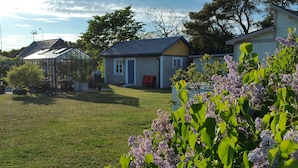 Ein Wohngebiet mit einem Haus, einem Gewächshaus und einem Garten voller blühender Blumen.