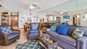 A spacious living room with a sofa, chairs, and a coffee table. There is a dining area with a table and chairs, and a kitchen in the background. - Stunning Oceanfront, 2BR/2BA, Gorgeous Ocean & Mt. Views, Premium A/C (Kihei)