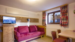 A cozy living room with a red sofa, wooden cabinet, and a television on a wooden stand.