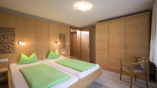 A room with two beds, wooden wardrobe, and a chair.