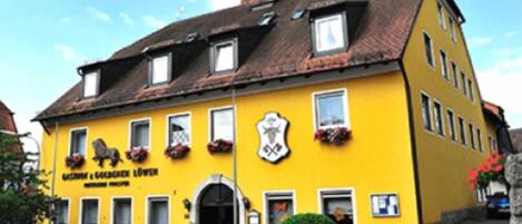 A yellow building with a black roof, multiple windows, and flower boxes.
