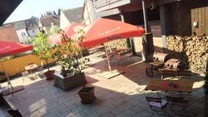 An outdoor patio area with tables and chairs, red umbrellas, and a stack of firewood. - Zum Goldenen Löwen (Moosbach)