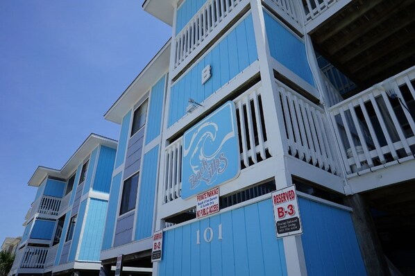 A multi-story building with a blue facade and white railings, featuring signs indicating private parking and reserved parking spaces. - Beachfront 3 Bedroom Condo at beautiful Ocean Isle Beach, NC (Ocean Isle Beach)