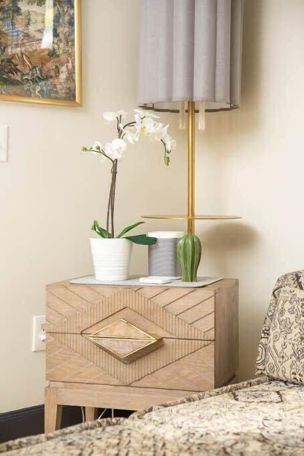 A wooden nightstand with a geometric drawer, a white orchid, and a green vase.