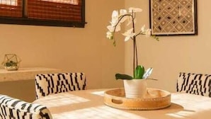 A round dining table with patterned chairs, a woven chandelier, a potted orchid, and a geometric wall art piece. - Boho Lux (Atlanta)