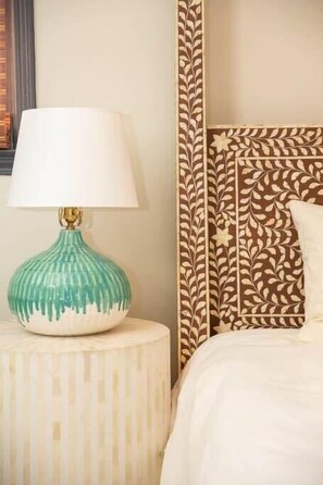 Una cama con cabecera estampada, una lámpara de noche y una almohada.