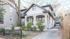 A two-story house with a brick facade, a front porch, and a driveway leading to a car parked in the driveway. - Boho Lux (Atlanta)
