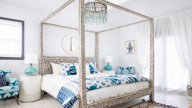 A four-poster bed with a patterned canopy, a round mirror, and a side table with a lamp. - Boho Lux (Atlanta)