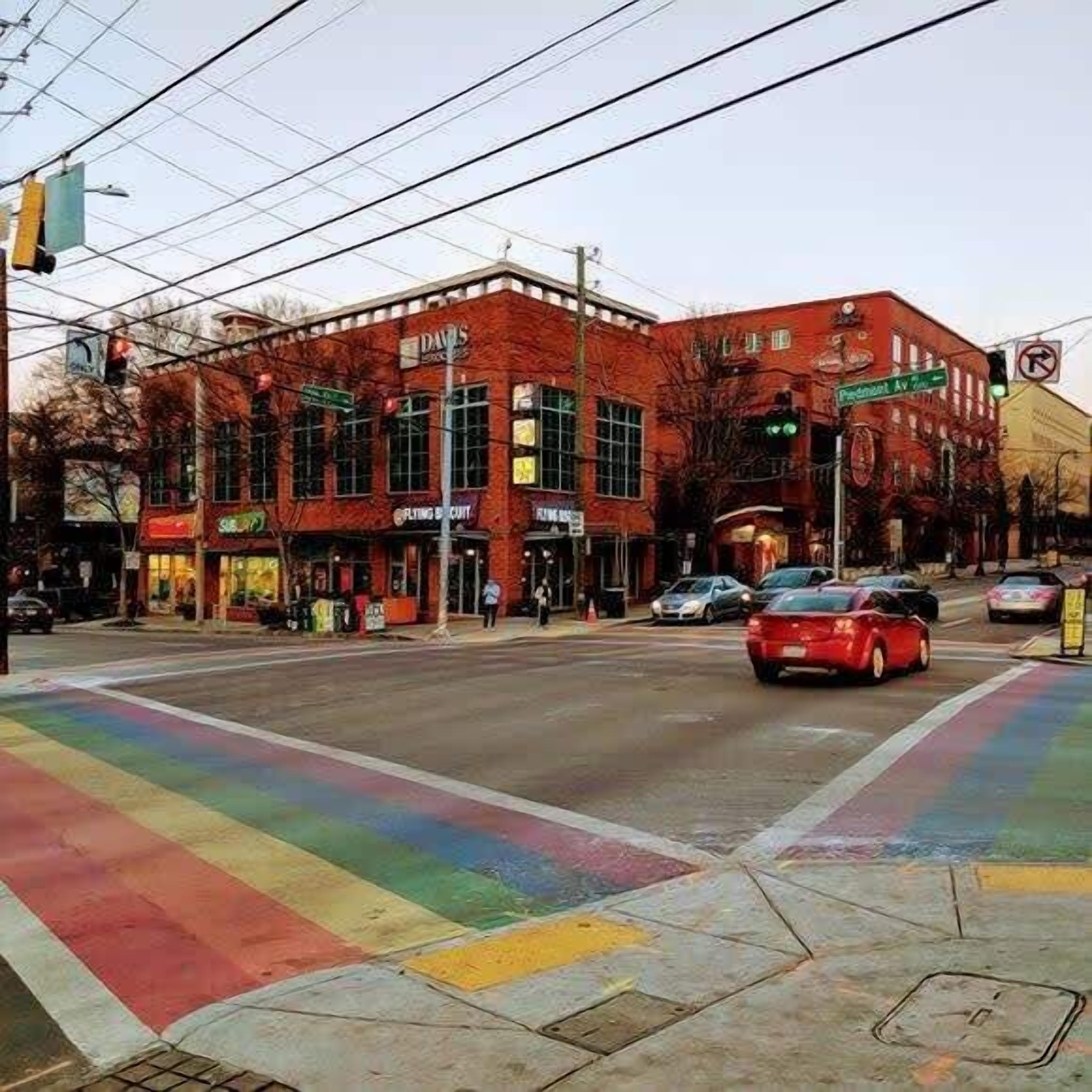 A street corner with a red brick building, a pedestrian crossing, and cars.